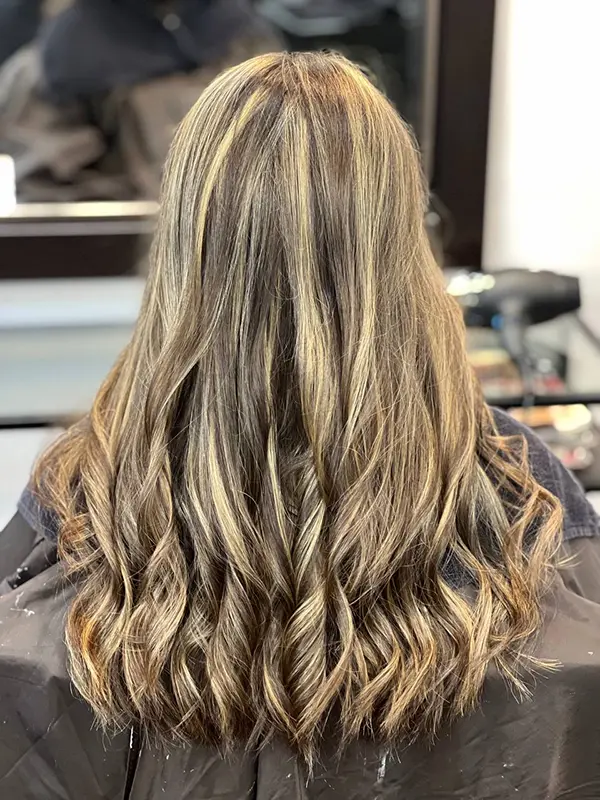 Dimensional blonde balayage on brunette hair with soft waves by CocoRez in Port Coquitlam.