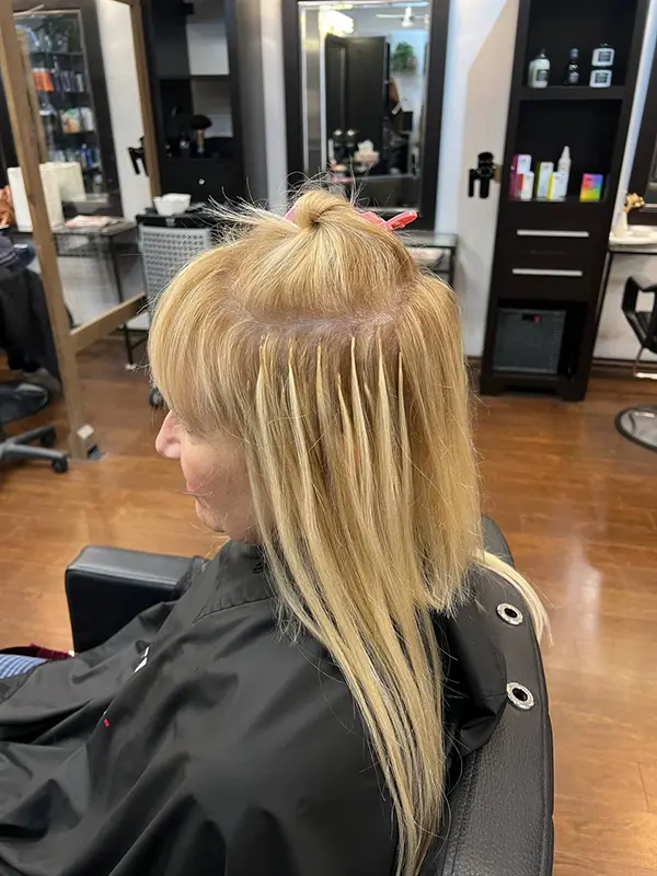 Keratin hair extensions being installed strand by strand on blonde hair at CocoRez in Port Coquitlam.